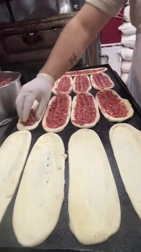 Tepsideki kayık hamurlara kıymalı harç elle yayılıyor